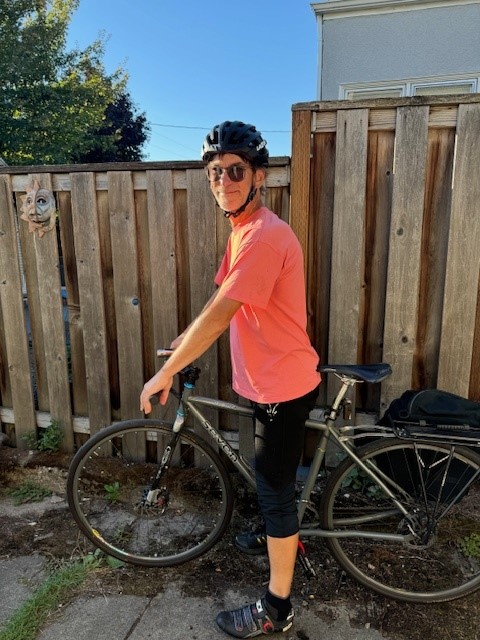 Hombre de pie con su bicicleta, con gafas de sol y una camiseta naranja.