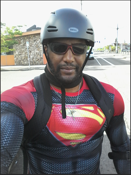 Hombre de pie con un casco de bicicleta y gafas de sol con una camiseta de superhéroe. 