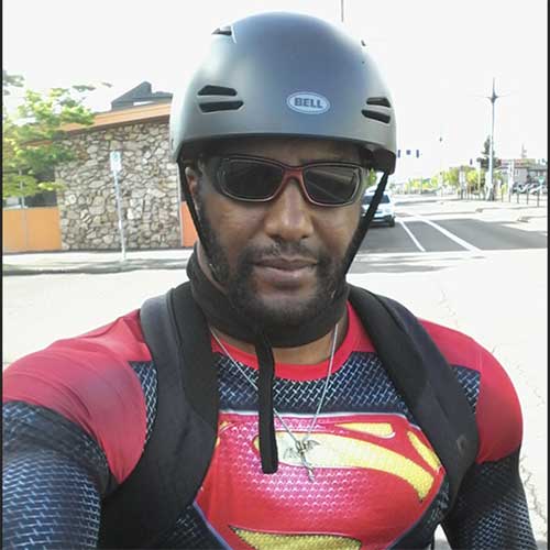 Man standing with a bike helmet and sunglasses in a superhero shirt.