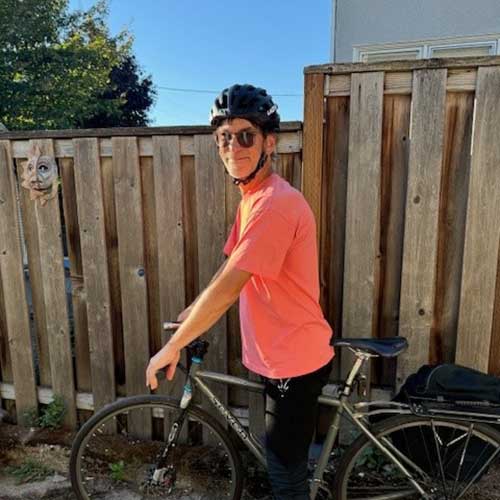 Man standing with his bicycle wearing sunglasses and an orange shirt.